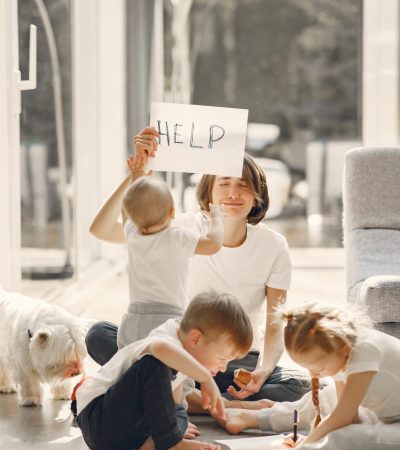 Stressed out parent with three young children holding up a sign saying 'help'